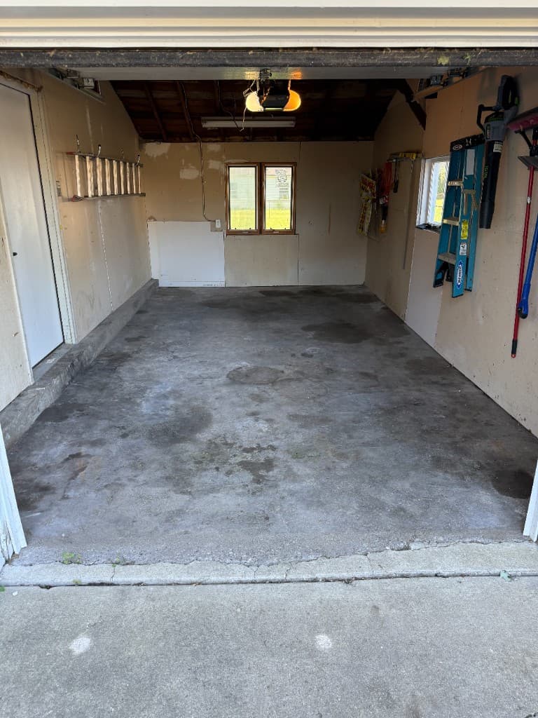 Before coating: worn stained concrete garage floor with unfinished walls.