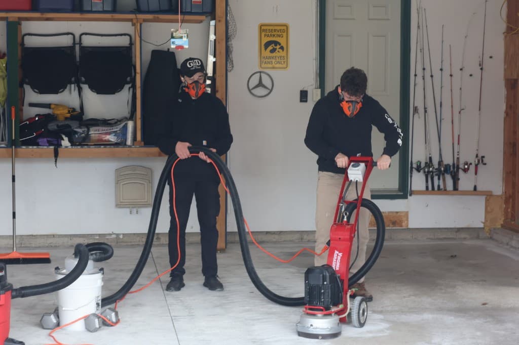 Two M-Pact workers grinding a garage floor with an industrial vacuum dust collection system.